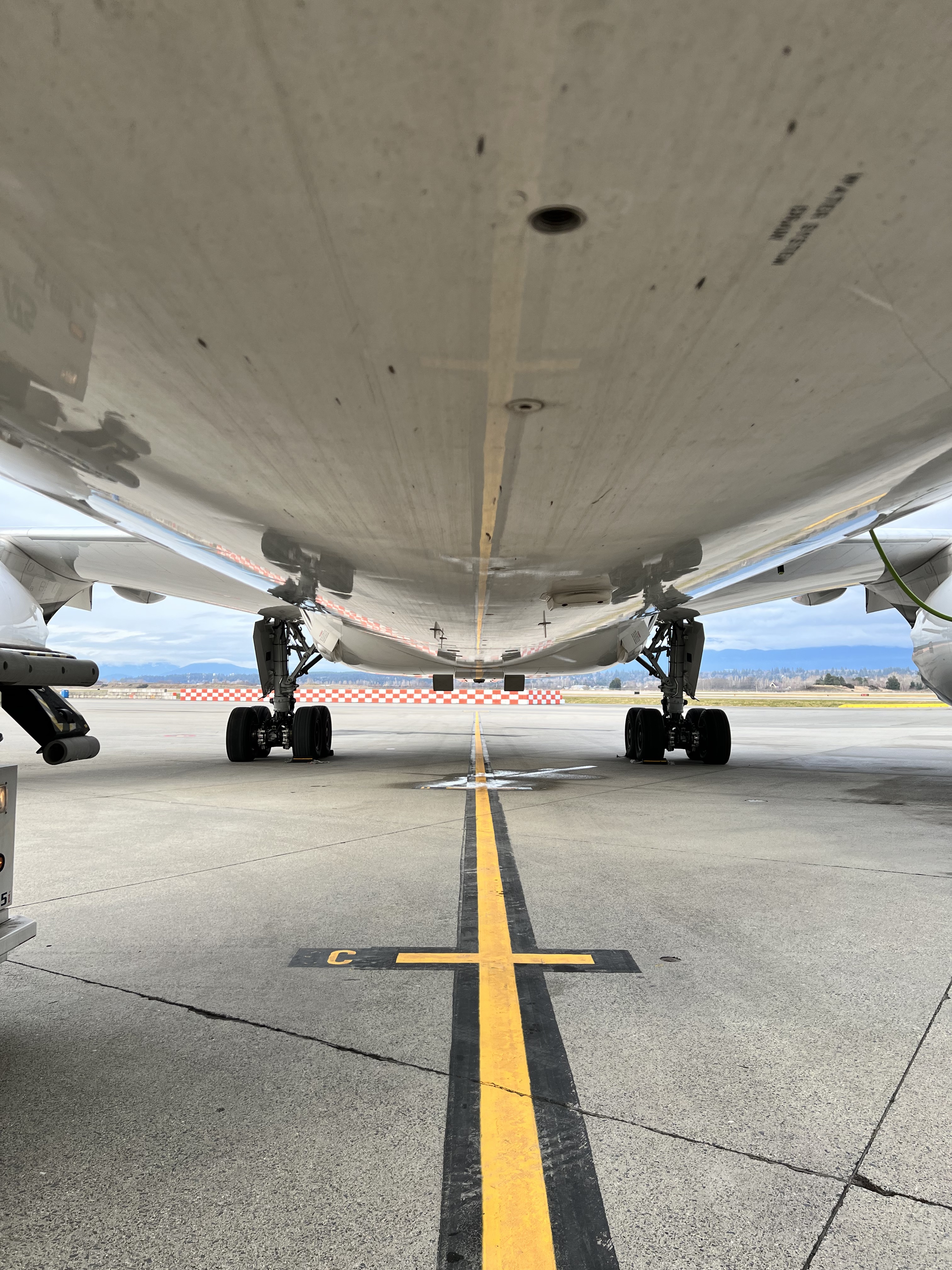 The photo shows the belly of an aircraft parked on a yellow line at the airport.